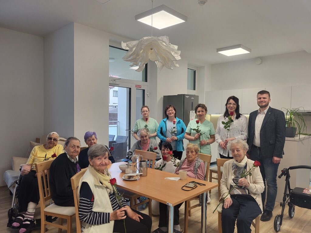 Obyvatelia domovu dôchodcov s personálom a primátorom s ružami v rukách