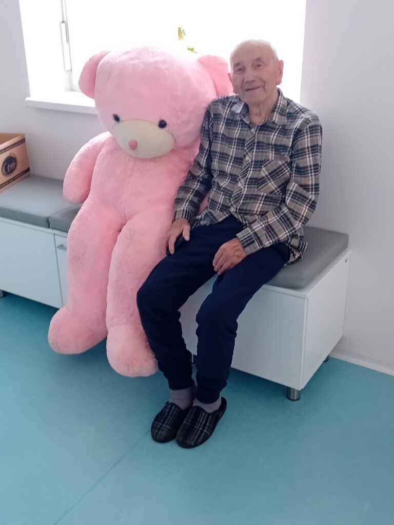 Dôchodca vedľa veľkého plyšového ružového medveďa v Harmónii