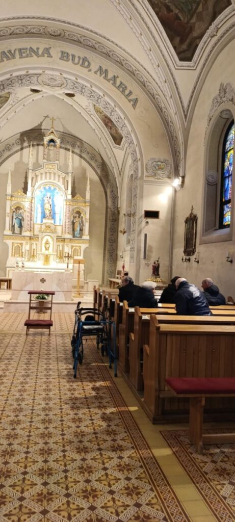 Interiér kostola so sediacimi ľudmi v laviciach