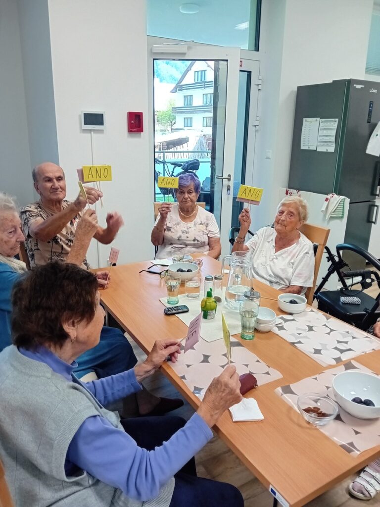 Seniori hlasujú kartičkami „áno“ a „nie“ počas skupinovej kognitívnej aktivity v zariadení Harmónia