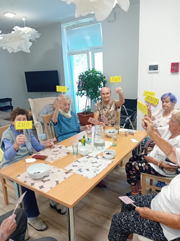 Seniori hlasujú kartičkami „áno“ a „nie“ počas skupinovej kognitívnej aktivity v zariadení Harmónia