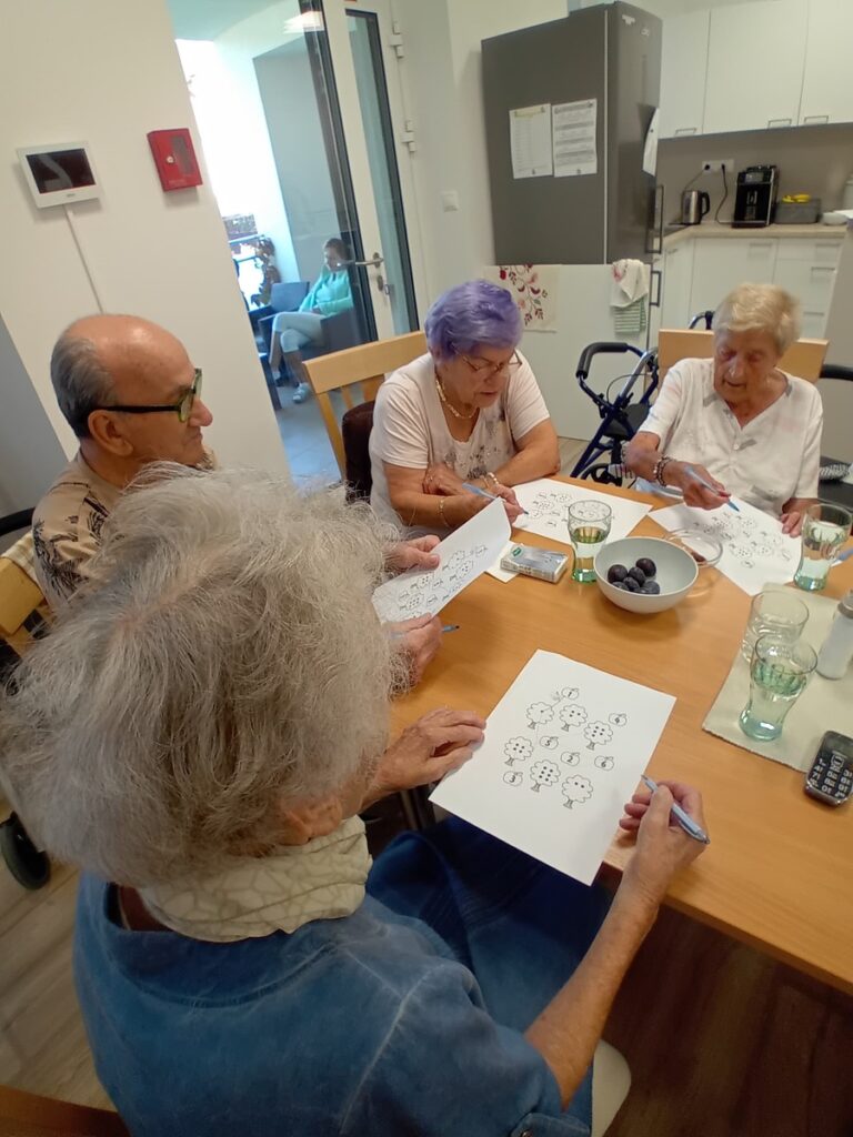 Spoločná práca seniorov na pracovných listoch pri stole v zariadení Harmónia