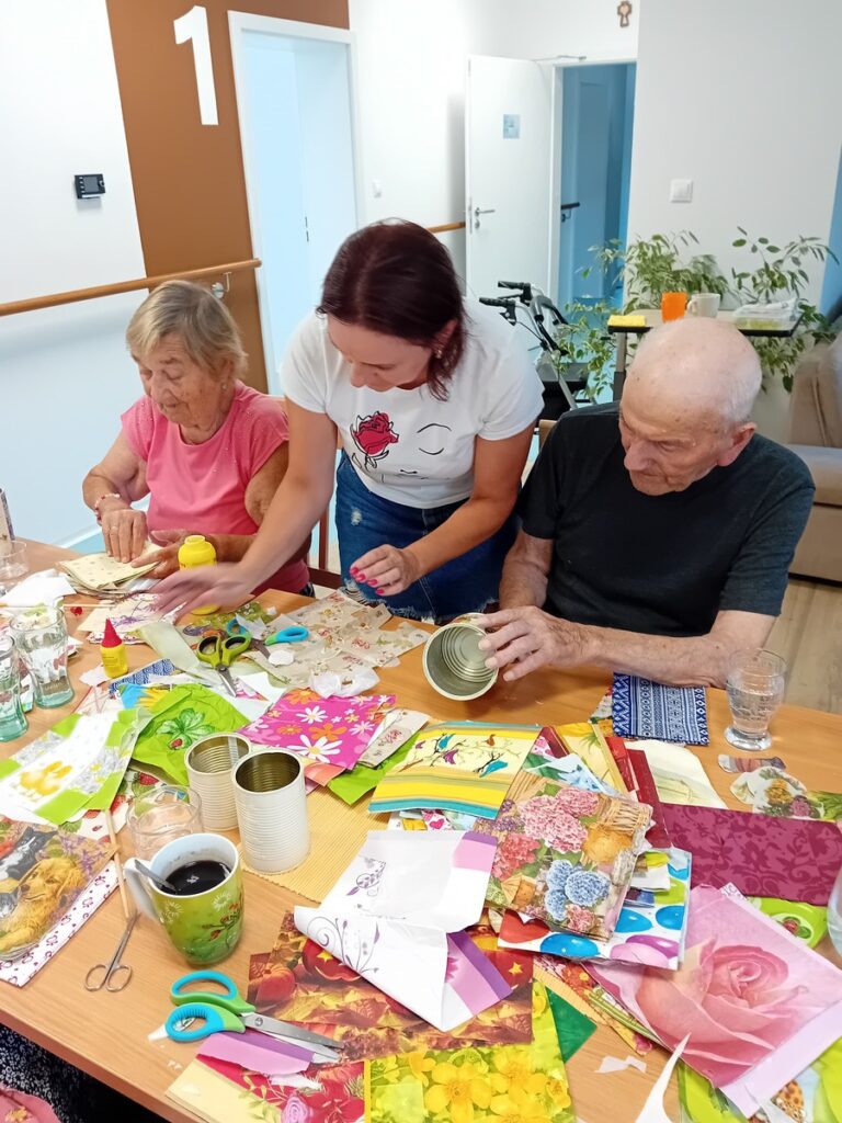 Opatrovateľka pomáha seniorom pri tvorivej aktivite v komunitnej miestnosti