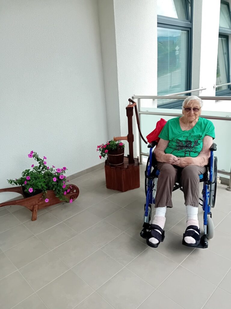 Senior na invalidnom vozíku oddychuje na terase zariadenia Harmónia obklopený kvetmi