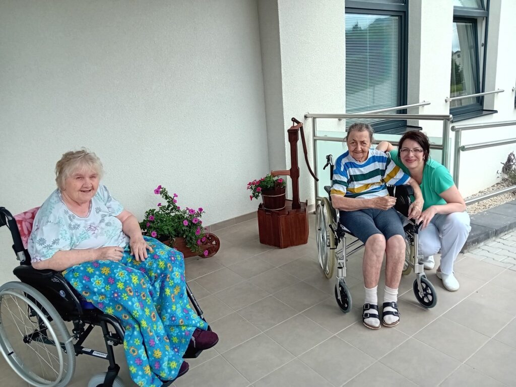 Seniori na terase zariadenia Harmónia spolu s opatrovateľkou počas letného posedenia