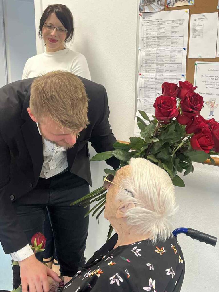 Odovzdávanie ruže seniorke počas slávnostnej návštevy v zariadení Harmónia