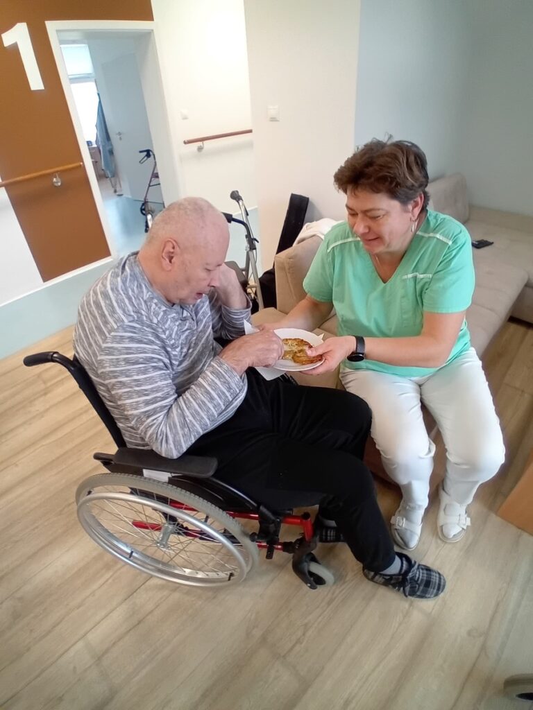 Opatrovateľka pomáha klientovi na invalidnom vozíku pri podávaní jedla